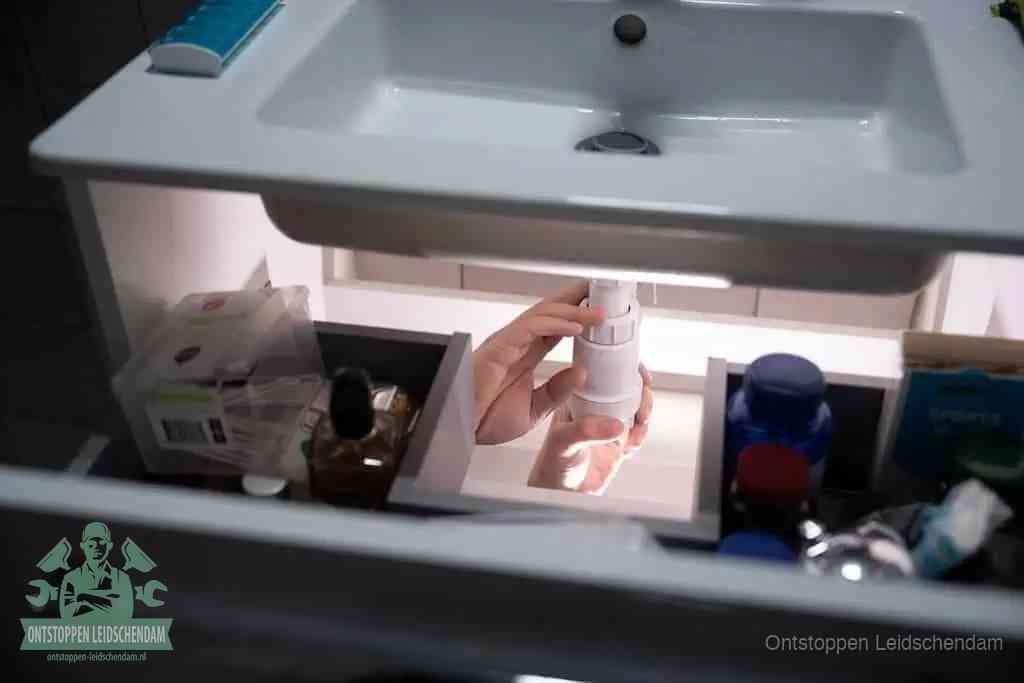 Een pompfles met zeep boven een wastafel, de heet water en afwasmiddel-methode om een vetprop in de afvoer los te maken in Leidschendam
