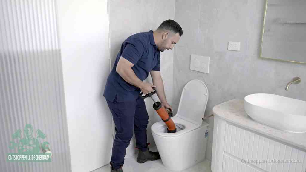 Een monteur buigt over een wandcloset en duwt met de hand een persluchtontstopper in de toiletpot om de verstopping handmatig los te maken in Leidschendam