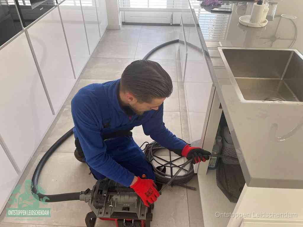 Een monteur ontstopt de keukenafvoer onder de spoelbak met een elektrische veermachine in Leidschendam