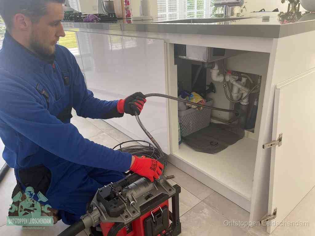 Monteur voert een ontstoppingsveer in de afvoer onder de keuken in Leidschendam