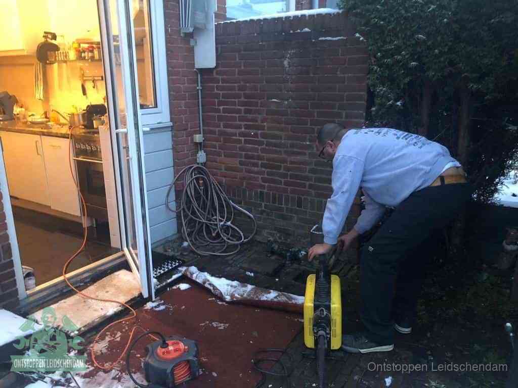 Een monteur werkt buiten bij een open riool-/grondput met een elektrische ontstoppingsmachine om een verborgen afvoerprobleem op te sporen in Leidschendam