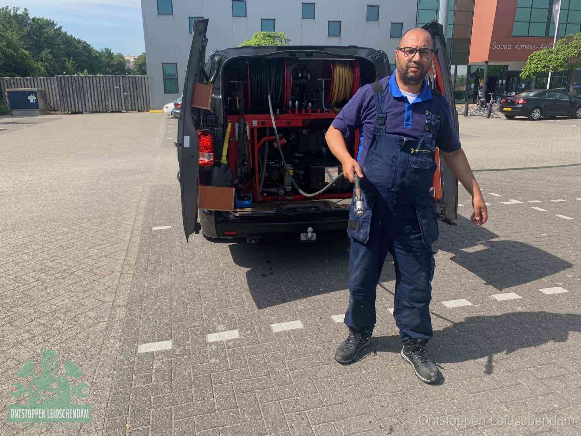 Een monteur bij zijn bestelbus met een hogedruk- en rioolreinigingsunit, klaar om de oorzaak van terugkerende wc-verstoppingen aan te pakken in Leidschendam