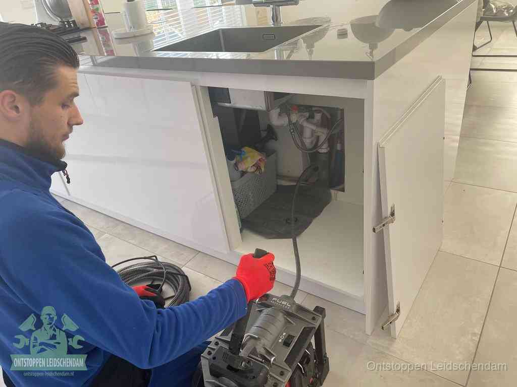 Monteur ontstopt met een veermachine een verstopte afvoer onder de gootsteen in Leidschendam
