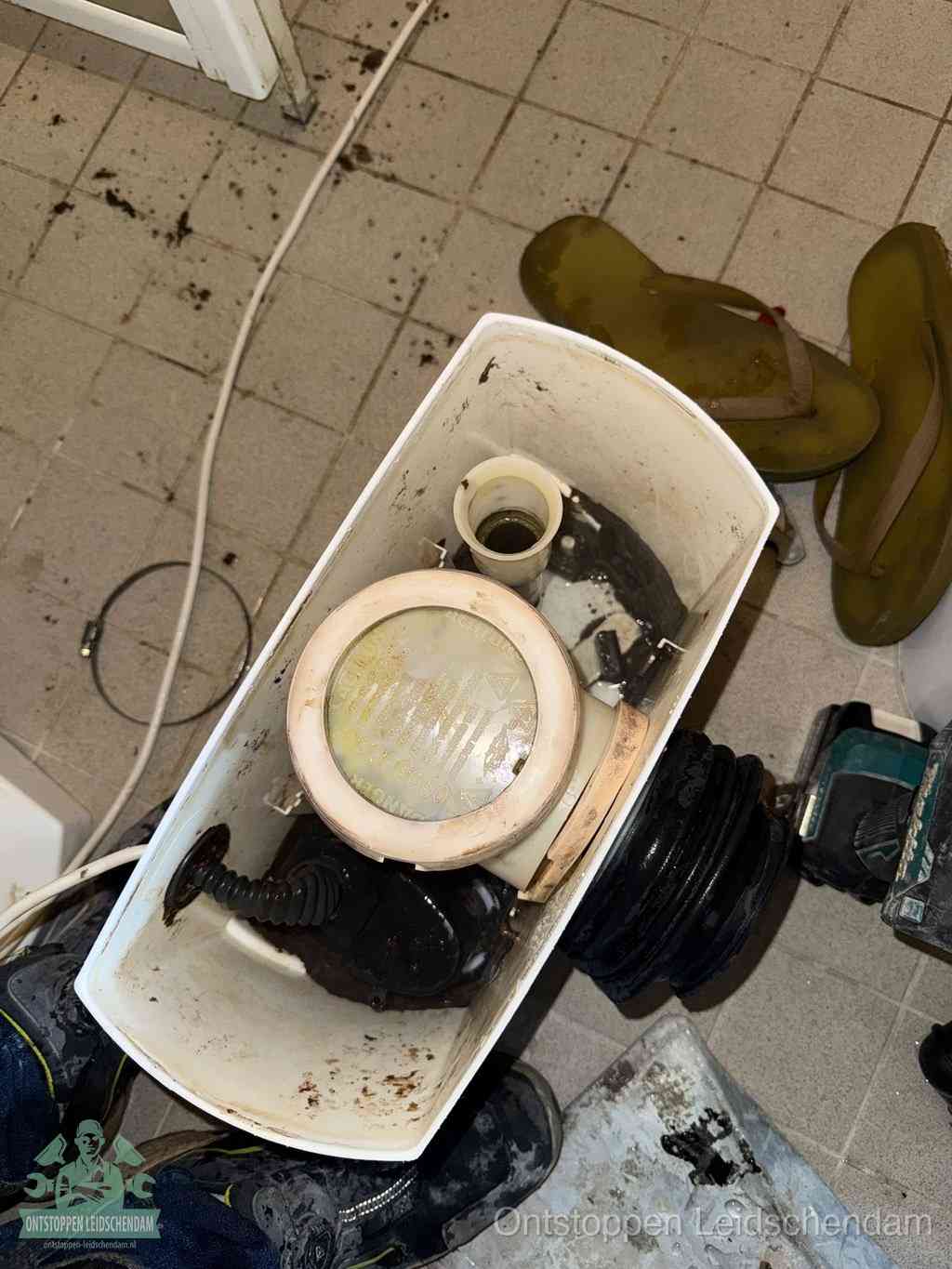 Een gedemonteerde toiletpot op de vloer met ontstoppingsveer en gereedschap ernaast, het verwijderen van een vastzittend voorwerp uit de wc in Leidschendam