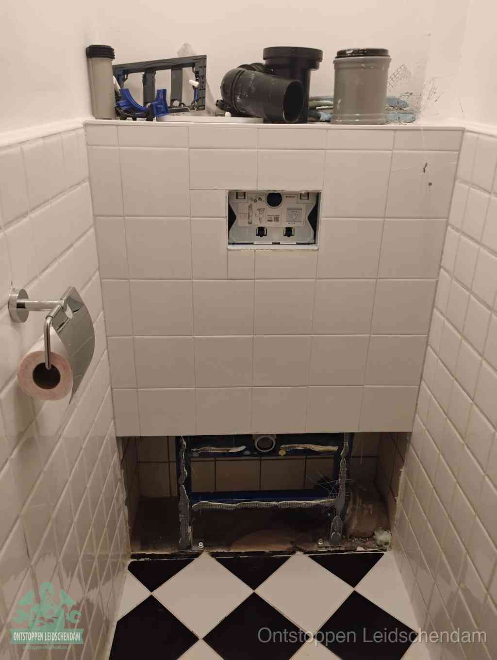 Een toiletruimte waar het hangtoilet en de inbouwreservoir-onderdelen zijn vrijgelegd voor onderhoud, periodiek nazicht voorkomt een wc-verstopping in Leidschendam