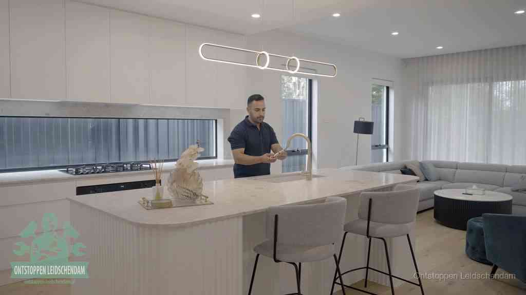 Een bewoner bij de keukenspoelbak die zelf aan de slag gaat met een verstopte gootsteen in Leidschendam