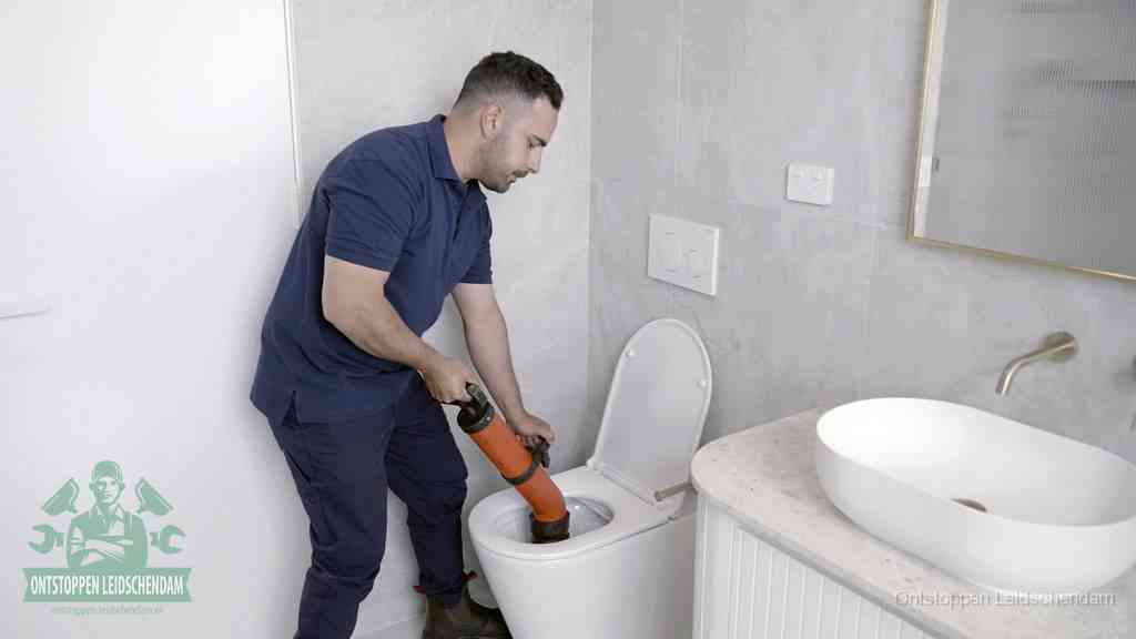Een man gebruikt een handmatige luchtdruk-ontstopper in een modern betegeld toilet om zelf de wc te ontstoppen in Leidschendam